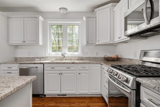 kitchen with white cabinets, a sink, stainless steel appliances, visible vents, and dark wood-style floors