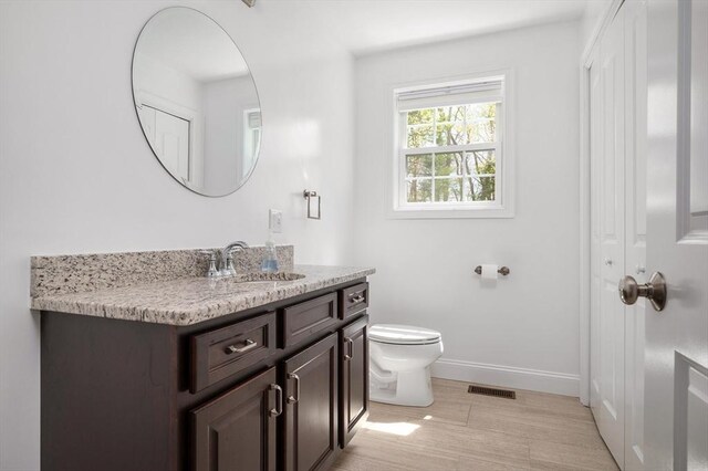 bathroom featuring vanity, toilet, baseboards, wood finished floors, and visible vents