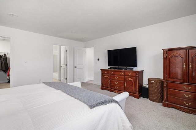 bedroom with light colored carpet and a walk in closet