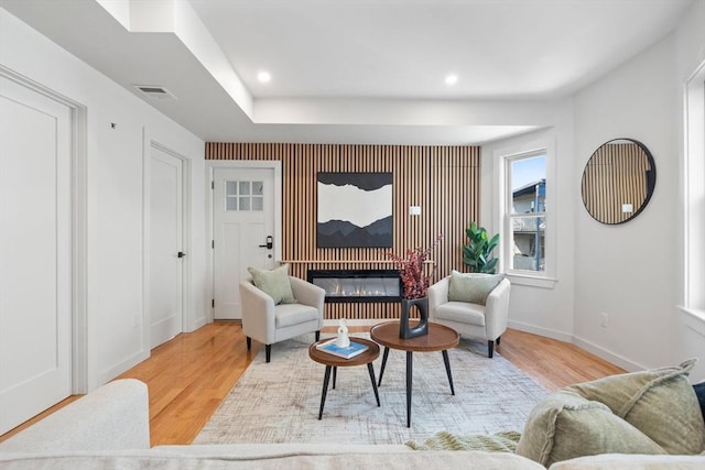 living area featuring a glass covered fireplace, visible vents, baseboards, and wood finished floors