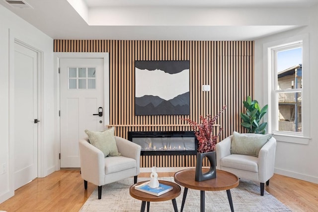 sitting room featuring a glass covered fireplace, baseboards, visible vents, and light wood finished floors