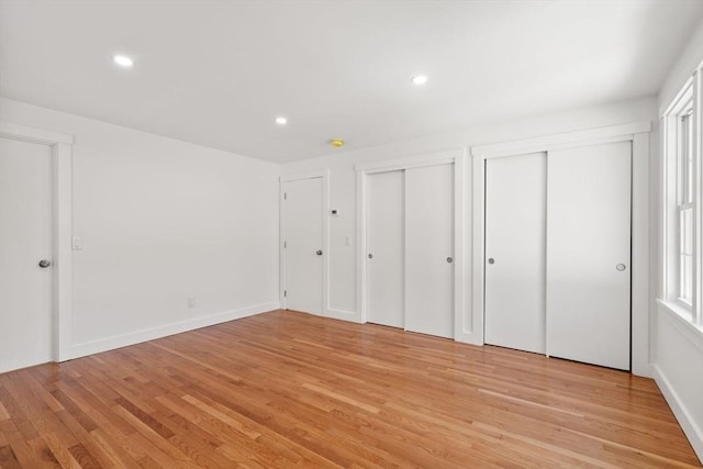 unfurnished bedroom featuring baseboards, recessed lighting, two closets, and light wood-style floors