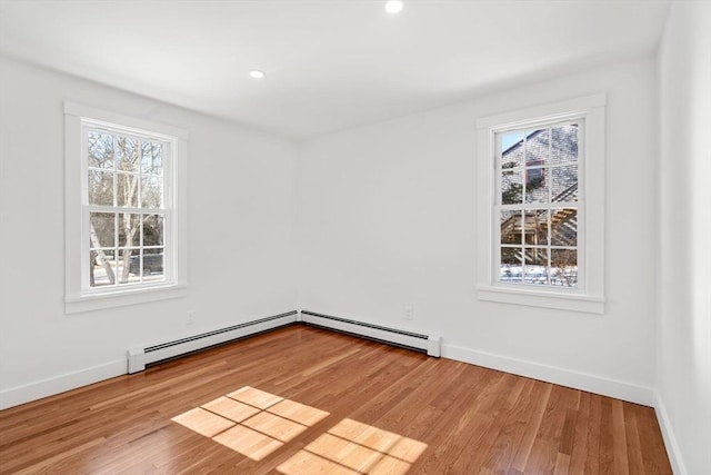 unfurnished room with a baseboard heating unit, baseboards, and wood finished floors