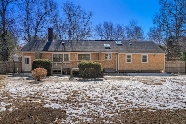 snow covered house with fence, a chimney, and a wooden deck