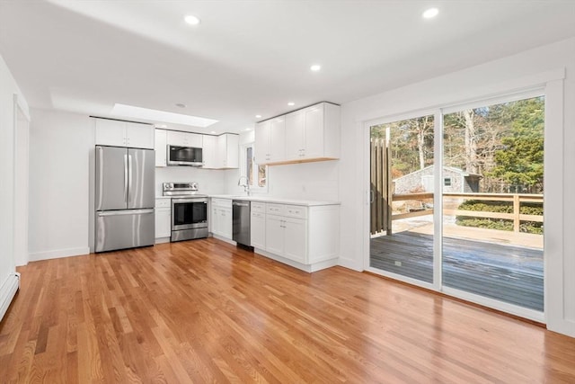 kitchen with appliances with stainless steel finishes, light countertops, light wood-type flooring, and white cabinetry