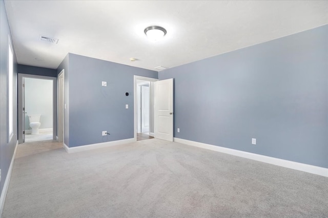 unfurnished bedroom featuring light carpet and ensuite bath