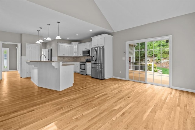 kitchen featuring appliances with stainless steel finishes, a kitchen bar, white cabinetry, light wood-style floors, and vaulted ceiling