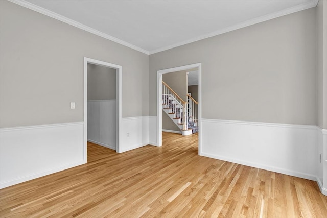 empty room with light wood-style floors, crown molding, stairway, and baseboards