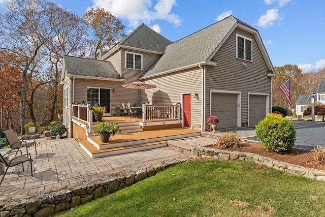 rear view of property with a wooden deck, an attached garage, a shingled roof, and driveway