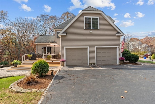 view of front of property featuring driveway, a garage, a wooden deck, and roof with shingles