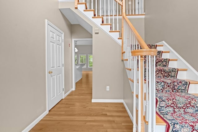 stairs featuring wood finished floors, baseboards, and a towering ceiling