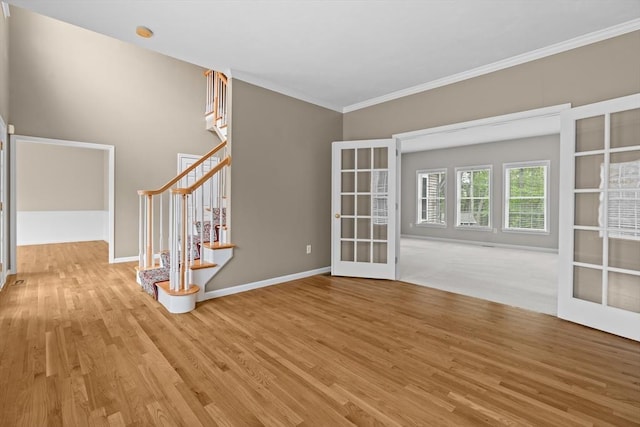 unfurnished room with french doors, wood finished floors, crown molding, baseboards, and stairs