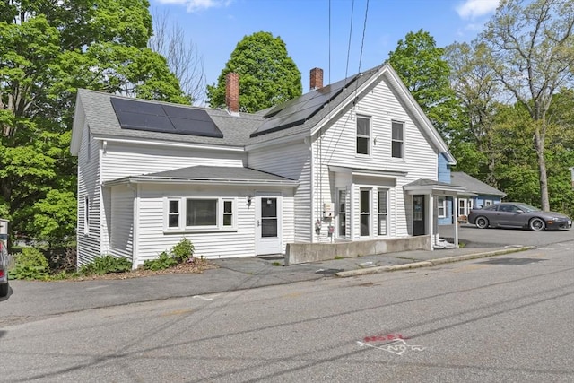 10 Jackson St, Ayer, MA 01432 - view of front of property with a chimney, roof mounted solar panels, and a shingled roof