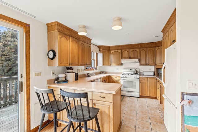 kitchen featuring sink, kitchen peninsula, a breakfast bar area, light tile patterned floors, and white appliances