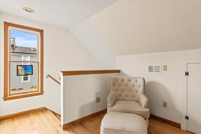 sitting room with light hardwood / wood-style floors, a textured ceiling, and vaulted ceiling