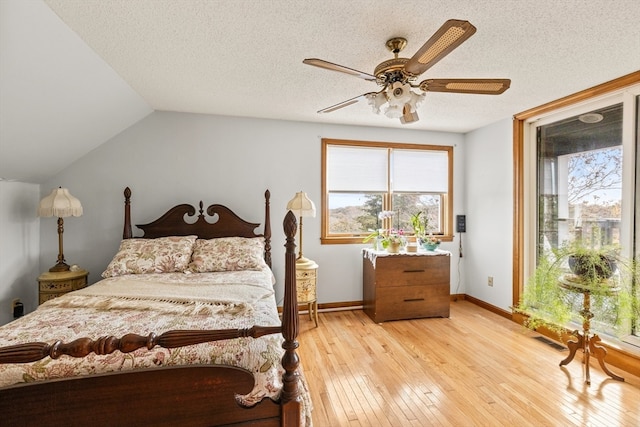 bedroom with a textured ceiling, light wood-type flooring, lofted ceiling, and ceiling fan