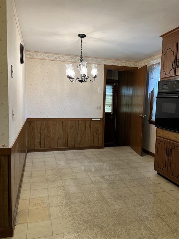 50 Feltham Rd, Springfield, MA 01118 - unfurnished dining area featuring wainscoting, a chandelier, wood walls, wallpapered walls, and light floors