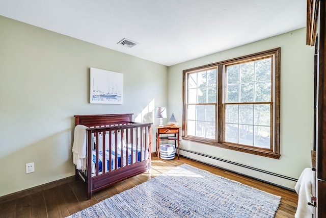 bedroom featuring a crib, hardwood / wood-style floors, and baseboard heating