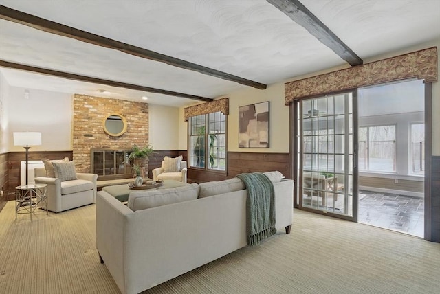 living area with a brick fireplace, beamed ceiling, wainscoting, and light carpet