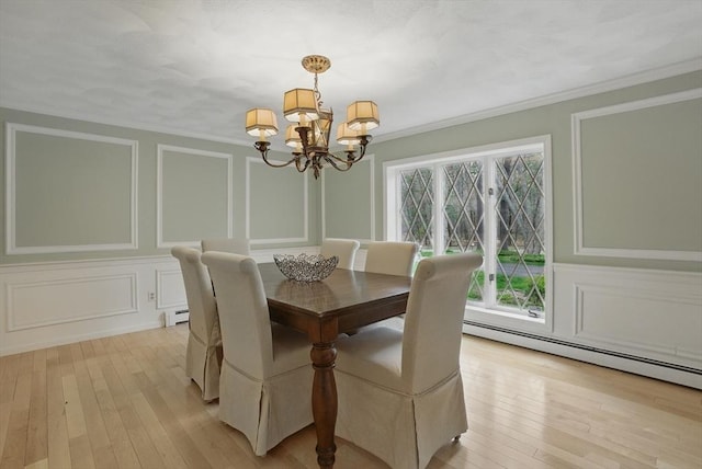 dining room featuring crown molding, light wood finished floors, a decorative wall, a chandelier, and a baseboard heating unit