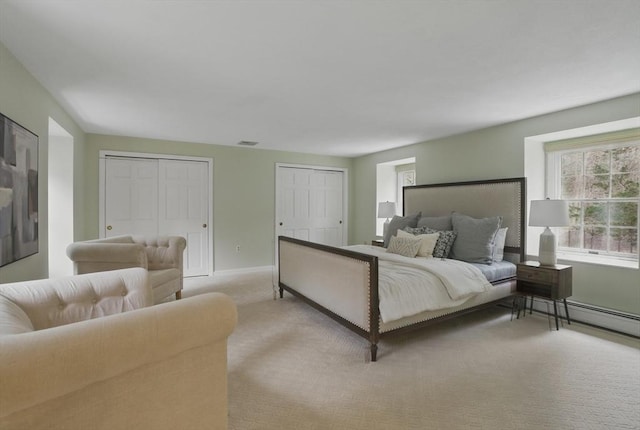 bedroom featuring light carpet, baseboard heating, two closets, baseboards, and visible vents