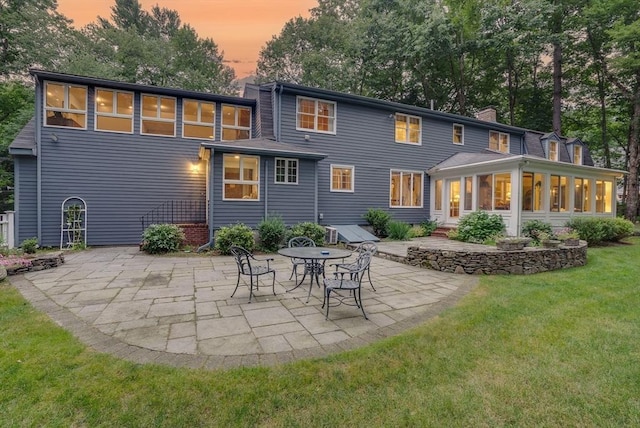 rear view of property with a yard, a sunroom, a chimney, and a patio area