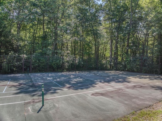 view of sport court featuring fence and a view of trees