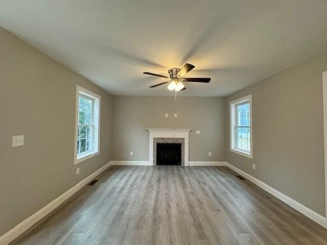 unfurnished living room with ceiling fan, light wood-type flooring, a fireplace, and baseboards