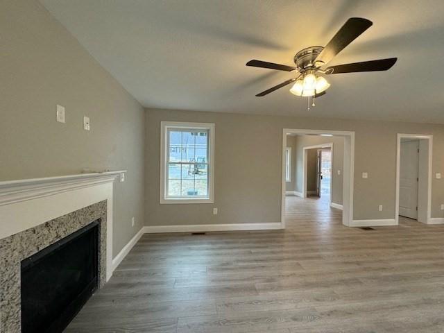 unfurnished living room with light wood-type flooring, a fireplace, a ceiling fan, and baseboards