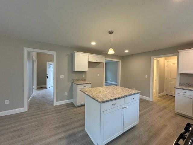 kitchen with light wood-type flooring, a kitchen island, decorative light fixtures, and white cabinets