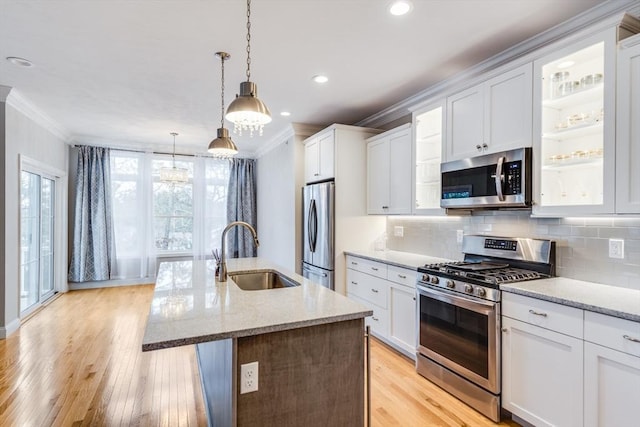 kitchen with a sink, appliances with stainless steel finishes, ornamental molding, and light wood finished floors