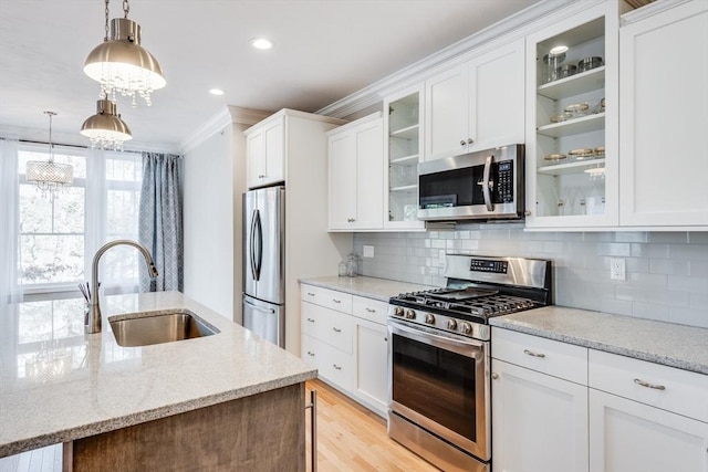 kitchen with a sink, ornamental molding, stainless steel appliances, light wood-style floors, and white cabinetry