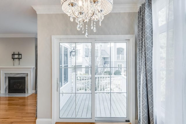 doorway to outside with wood finished floors, an inviting chandelier, a fireplace, and crown molding