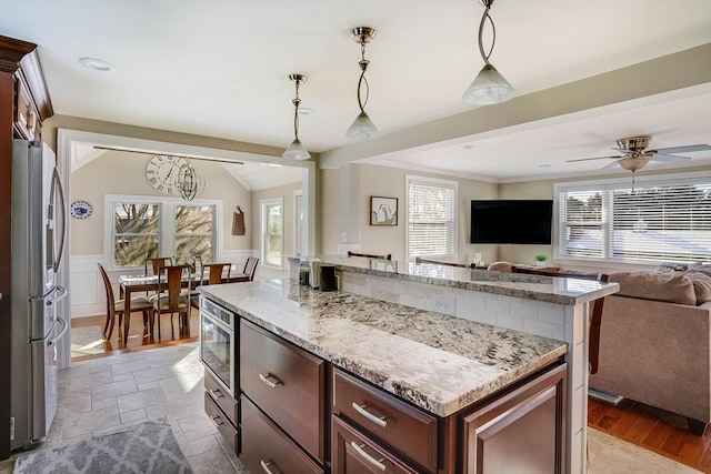 kitchen featuring stainless steel appliances, decorative light fixtures, vaulted ceiling, a kitchen island, and light stone counters