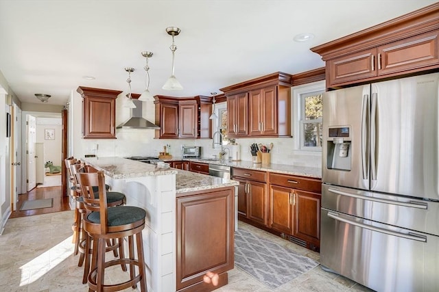 kitchen featuring a kitchen island, hanging light fixtures, appliances with stainless steel finishes, wall chimney exhaust hood, and light stone counters