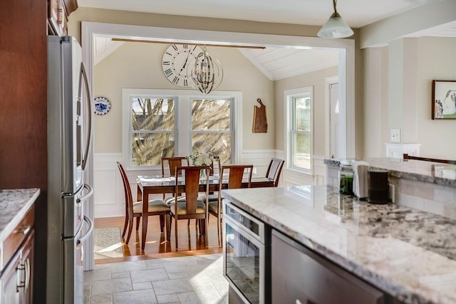 kitchen with an inviting chandelier, stainless steel fridge, decorative light fixtures, vaulted ceiling, and light stone counters