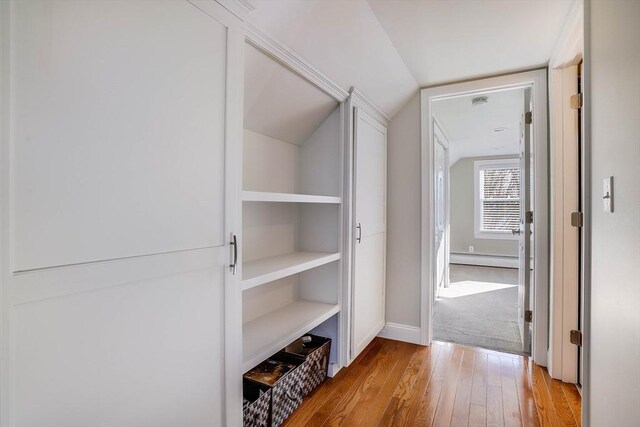 corridor with vaulted ceiling, a baseboard heating unit, and light hardwood / wood-style flooring