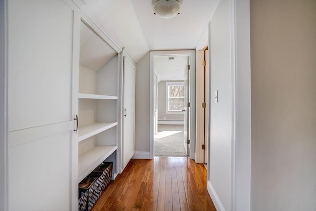 corridor featuring baseboard heating, vaulted ceiling, built in features, and wood-type flooring