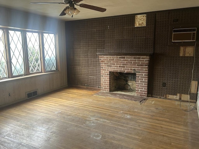 unfurnished living room featuring ceiling fan, light wood-type flooring, a wall unit AC, and a fireplace