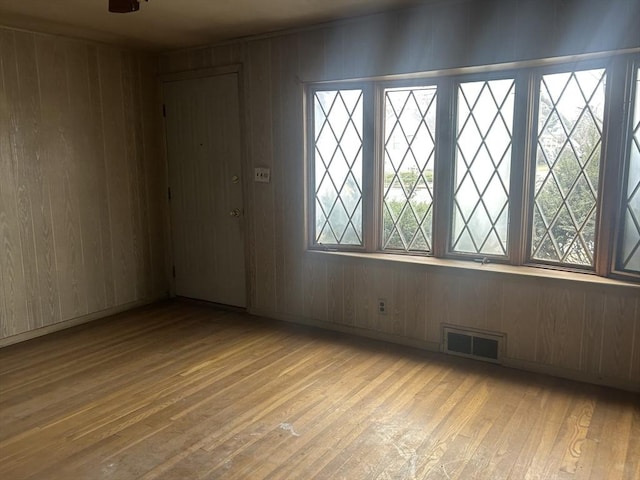 unfurnished room with light wood-type flooring, ceiling fan, and wooden walls