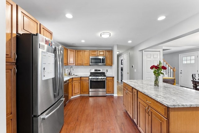 kitchen featuring decorative backsplash, brown cabinets, wood finished floors, stainless steel appliances, and a sink