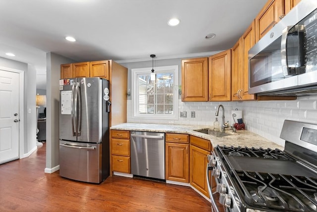 kitchen with stainless steel appliances, hanging light fixtures, brown cabinetry, a sink, and light stone countertops