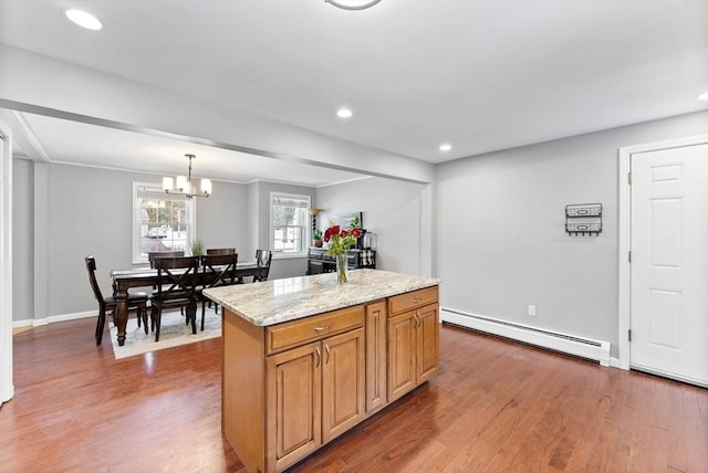 kitchen with light stone counters, dark wood finished floors, a baseboard heating unit, brown cabinetry, and a kitchen island with sink