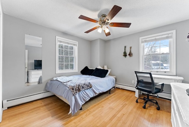 bedroom featuring a baseboard heating unit, a textured ceiling, wood-type flooring, and a ceiling fan