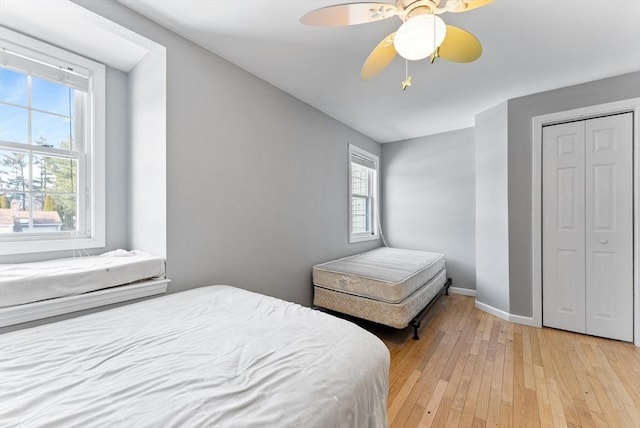 bedroom featuring a ceiling fan, a closet, light wood-style flooring, and baseboards