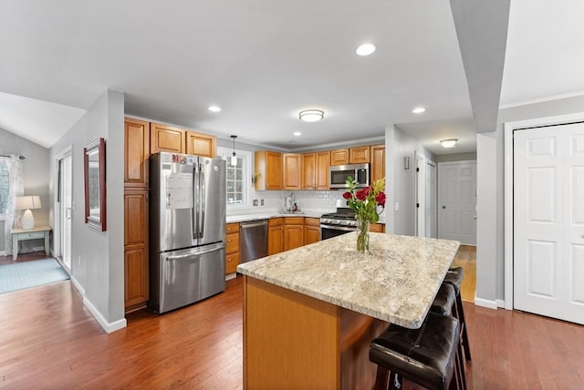 kitchen with a breakfast bar area, dark wood-type flooring, decorative light fixtures, a center island, and stainless steel appliances