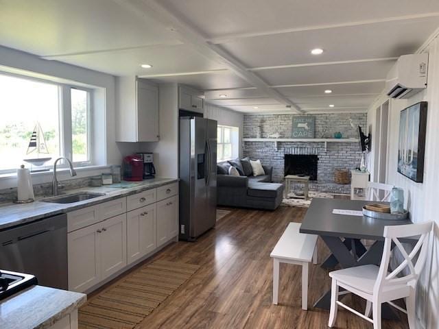 kitchen with stainless steel refrigerator with ice dispenser, a wall unit AC, a sink, dishwasher, and plenty of natural light