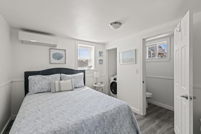 bedroom with a wall unit AC, washer / dryer, wood finished floors, and wainscoting