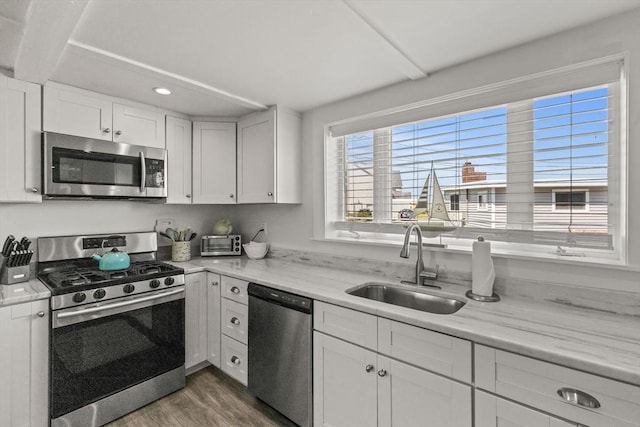 kitchen featuring appliances with stainless steel finishes, a sink, wood finished floors, white cabinets, and recessed lighting