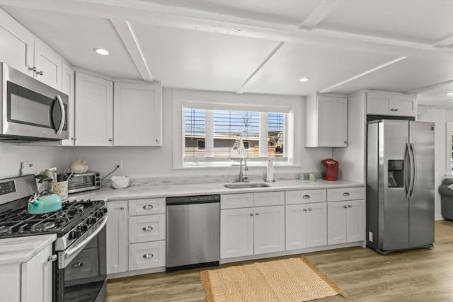 kitchen featuring stainless steel appliances, a sink, light countertops, white cabinetry, and light wood-style floors